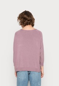 Lavenderfarbener Strickpullover mit lockerer Passform, dreiviertellangen Ärmeln und rundem Ausschnitt, kombiniert mit hellblauen, verwaschenen Jeans.