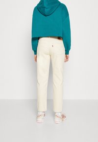 Teal cropped hoodie with a hood, paired with cream-colored straight-leg jeans. Sneakers feature a multicolor design and visible branding.