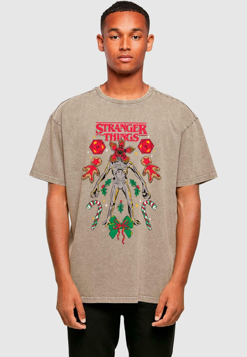 Hnědý bavlněný tričko s barevným grafikou „Stranger Things“, zobrazující postavu obklopenou prvky s vánoční tématikou a cukrovými tyčinkami.