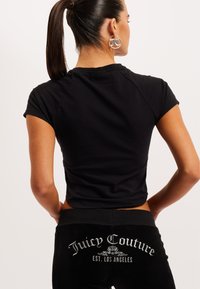 Čierny priliehavý top s krátkym rukávom je skombinovaný s čiernymi zamatovými teplákmi so strieborným logom "Juicy Couture" na zadnej strane a jemným leskom.