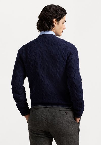 Pull en maille torsadée marine à col rond et ourlet côtelé, accompagné d'un pantalon gris anthracite, affichant un tissu texturé.