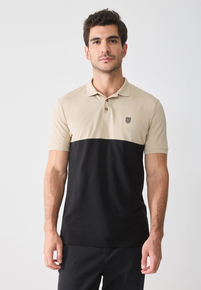 Polo in beige e nero, con maniche corte, colletto, tre bottoni e un logo applicato sulla parte sinistra del petto.