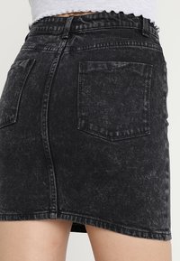 Minifalda de denim negro con un lavado desgastado, con un bolsillo trasero, dobladillo deshilachado y costuras de contraste.