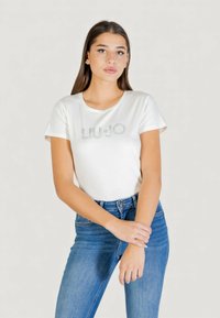 Biała koszulka z krótkim rękawem wykonana z bawełny, z logo "LIU•JO" zdobionym połyskującymi detalami na przodzie. Połączona z niebieskimi dżinsami.