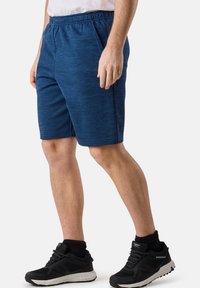 Marinblå atletiska shorts med strukturerad tyg, elastisk midja och sidofickor, kombinerat med svarta atletiska skor och ankelsockor.