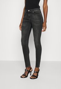 Jeans negros ajustados de mezclilla con bolsillos frontales, textura suave y costuras visibles. Combinados con sandalias negras de tacón.