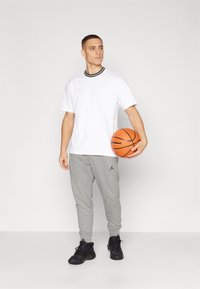 Hvit sports T-skjorte med svart ribbestrikket krage, kombinert med grå treningsbukser med svart Jordan-logo. Svarte joggesko og en basketball.