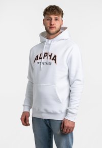 Sudadera blanca con bolsillo tipo canguro, cordones y el texto "ALPHA INDUSTRIES" en negro y naranja. Tejido suave y corte relajado.