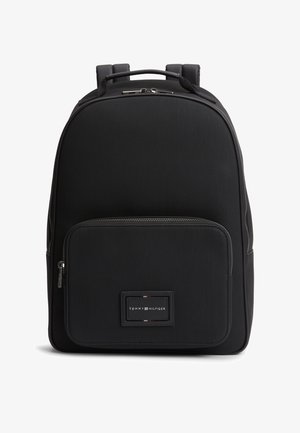Sac à dos noir Tommy Hilfiger avec poche avant zippée, poignée supérieure et bretelles, affichant le logo de la marque sur la poche avant.