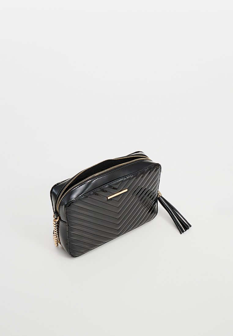 Pochette zippée en synthétique noire avec un motif en chevron, accents en métal doré et détail de glands sur le côté. Texture lisse avec finition brillante.
