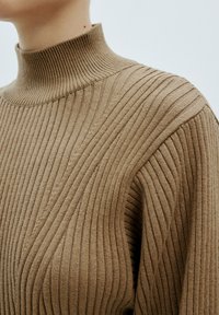Brauner gerippter Rollkragenpullover mit vertikalen Linien, der einen hohen Kragen und strukturierte Stoffe aufweist. Nahaufnahme, die die Stoffdetails zeigt.