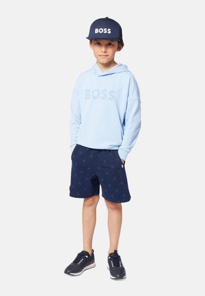 Felpa azzurra con logo "BOSS", pantaloni corti blu navy con motivo e cappellino blu navy con "BOSS". Sneakers nere completano l'outfit.