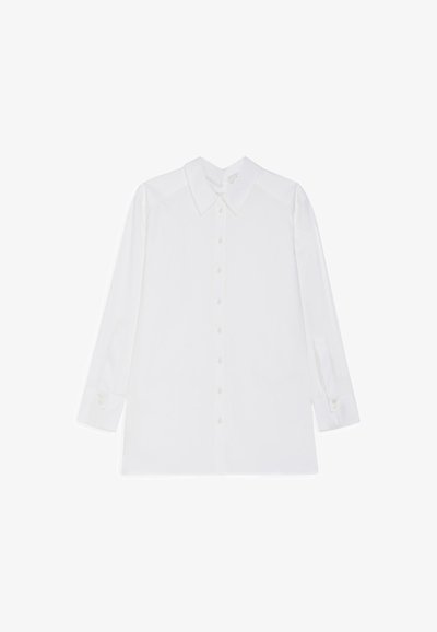 Bela dolga majica z dolgimi rokavi iz bombaža, ki ima klasičen ovratnik, zapenjanje spredaj na gumbe in zapete manšete, s nekoliko ohlapnim krojem.