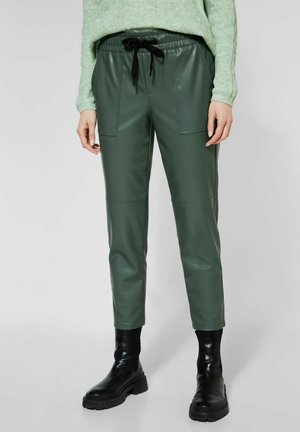 Pantalons en simili cuir vert avec une taille élastique, un cordon de serrage et des poches avant ; associés à des bottines noires pour un contraste.