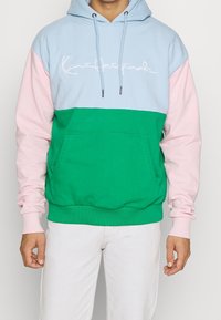 Felpa con cappuccio a blocchi di colore, con parte superiore azzurro chiaro, maniche rosa e corpo verde. Include una tasca frontale e cappuccio regolabile con cordino.