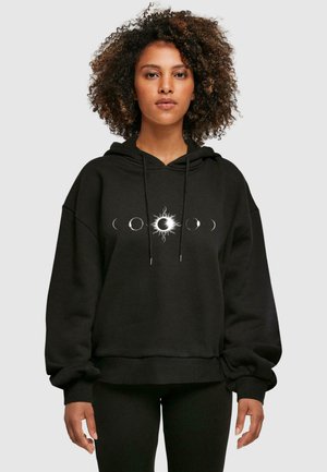 Black oversized hoodie featuring a circular sun and moon graphic in white, with a drawstring hood and ribbed cuffs and hem.