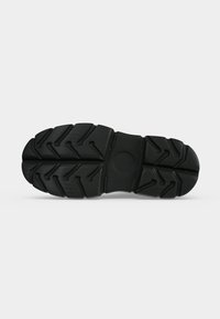 Semelle de chaussure noire robuste avec des rainures profondes multidirectionnelles et un motif circulaire au centre pour l’adhérence et la stabilité.