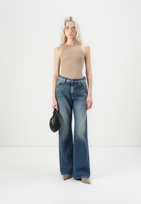 Beige aansluitend tanktop gecombineerd met hoge taille blauwe wijde-spijkerbroek, met een zwarte clutch; gladde stof en gestructureerd ontwerp.