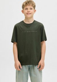 Tamsiai žalia medvilninė marškinėliai trumpomis rankovėmis ir apvaliu kaklu, puošiami balta "JACK & JONES" tekstu krūtinėje. Dėvimi su šviesaus džinsinio audinio kelnėmis.