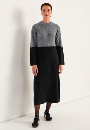 Langes Sweaterkleid mit grauem Oberteil und schwarzem Unterteil, aus weichem Material gefertigt. Es hat einen runden Halsausschnitt und lange Ärmel.