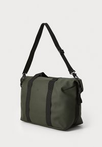 Olivengrønn duffelbag laget av slitesterkt materiale, med svarte polyesterstropper, glidelås og rektangulær form.