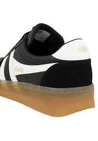 Sneaker in bianco e nero con tomaia in suede e pelle texture, dotata di suola in gomma naturale e accento dorato del logo sul tallone.
