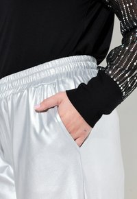 Silver satin joggers med elastisk midja, med en sidficka, tillsammans med en svart långärmad topp med genomskinlig paljettärm.