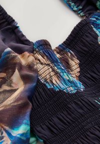 Flerfärgat tyg med en blandning av mörka nyanser och livliga blågröna accenter, med en texturerad smockdesign och detaljerat blommönster.