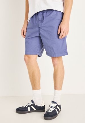 Leichte blaue Shorts mit elastischem Bund und Kordelzug, ausgestattet mit Seitentaschen und einem geraden Saum, getragen mit dunkelblauen Sneakers und weißen Socken.