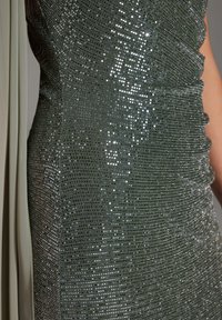 Funkelndes grünes Kleid mit Paillettenstruktur, gerafftem Design und einem fließenden, hellen Stoffakzent an der Seite.