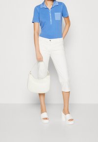 Blå polo skjorta med krage och knappslå, vita överknälånga byxor, vit handväska och plattformssandaler i vitt. Släta texturer genomgående.