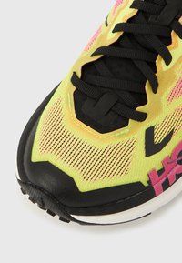 Bėgimo batelis su fluorescenciškai geltonu tinklelio viršumi, rožiniais akcentais, juodais raišteliais ir tekstūruotu juodu padu, skirtu sukibimui.