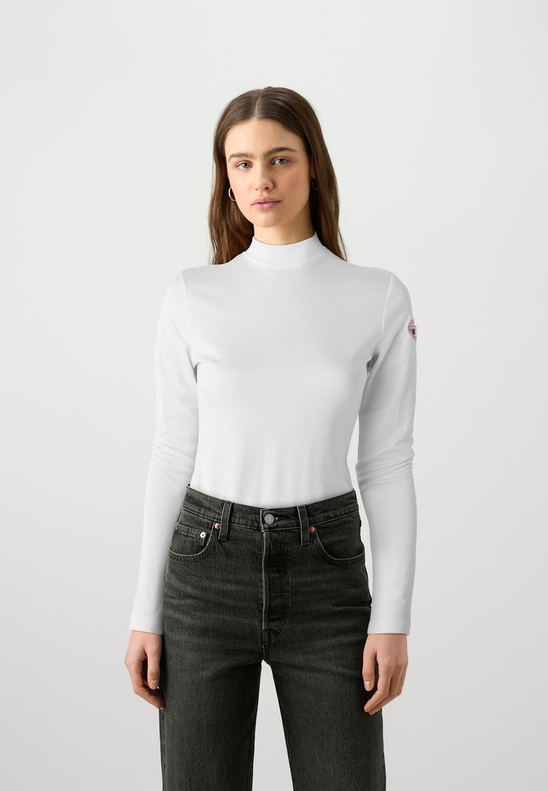 Hvit langermet turtleneck topp laget av glatt stoff, med en tettsittende design og rund hals, kombinert med mørke høyhalsede jeans.