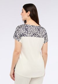 Lyhyet hihnat, joissa on kerma värinen vartalo ja kuvioitu tummansininen ja valkoinen takakappale, pehmeä kangas ja rento istuvuus.