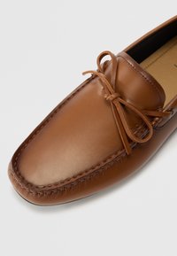 Brūni ādas loafers ar gludu faktūru, noapaļu purngalu un dekoratīvu sasietu loku. Iekļauj šuvju malās un melnu zoli.