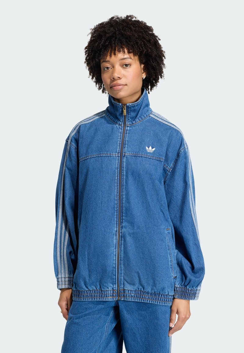 Veste en jean avec col montant, fermeture éclair et poignets élastiques. Présente trois bandes blanches le long des manches et un petit logo sur la poitrine.