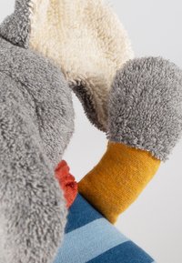 Morbido peluche con corpo grigio, orecchie bianche, gambe con righe colorate e un design testurizzato e soffice. Presenta un accento rosso e arancione.