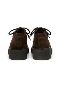 Chaussures en daim marron avec un profil bas, lacées de noir, et une semelle en caoutchouc texturé. Présente des détails en relief au niveau du talon arrière.