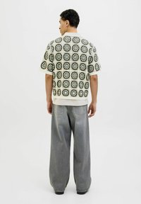 Majica s kratkimi rokavi z teksturiranim, vzorčastim dizajnom v zeleno-beli barvi, kombinirana s širšimi sivo-denim hlačami.