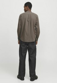 Brown long-sleeve shirt with a round collar, featuring button closures and a straight hem, paired with dark denim pants and black boots.