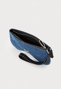 Denim kassi mustalla vetoketjulla, jossa on hopeinen yksityiskohta ja irrotettava ranneke. Sisäosa on vuorattu mustalla kankaalla.