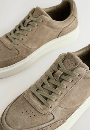 Pair of taupe suede sneakers with olive green laces and white rubber soles on a light background.