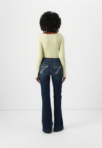 Light green ribbed long-sleeve top paired with dark denim flared jeans featuring distinctive stitching on the back pockets.