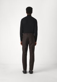 Sort genser i svart strikk og brune skreddersydde bukser, med en slim fit. Buksene har lommer og en glatt tekstur. Svarte sko fullfører antrekket.