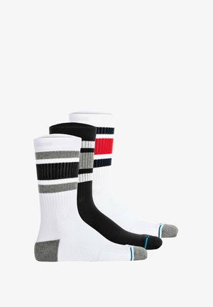 Drie paar crew-sokken: één witte met zwarte en rode strepen, één grijs met zwarte strepen, en één zwarte effen. Alle met ribbeltextuur.