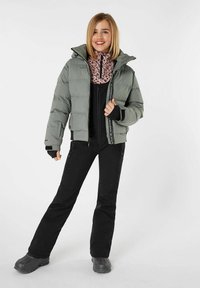 Lichtgrijze gevoerde jas met capuchon, zwarte rits en een roze dierenprintlaag eronder, gecombineerd met zwarte broek en zwarte schoenen.