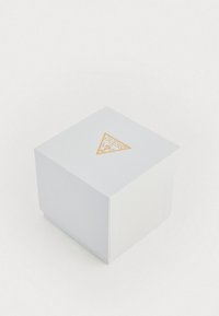 Bijela kvadratna kutija s teksturiranom površinom. Sadrži zlatni trokutasti logo na vrhu. Zatvorenog dizajna, minimalističkog i modernog izgleda.