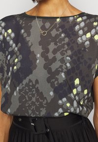 Krátký rukáv top v tmavé tkanině s vícebarevným vzorem v šedé, černé a s akcenty jasně žluté; hladká textura a uvolněný střih.