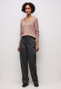 Hellrosa V-Ausschnitt Pullover kombiniert mit locker sitzenden grauen Nadelstreifenhosen. Das Outfit verfügt über lange Ärmel und einen Knopfverschluss in der Taille.