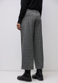 Harmaat herringbone-kuosiset leveälahkeiset housut, joissa on korkea vyötärö, hieman teksturoitu kangas ja sivutaskut, yhdistettynä mustiin nilkkureihin.